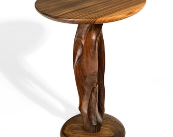 May include: A handcrafted wooden side table with a round top and a uniquely carved base. The table is made of dark brown wood, showcasing the natural grain. The table's top is approximately 18 inches in diameter.