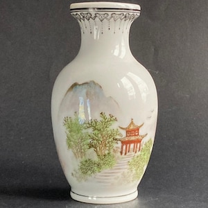 May include: White porcelain vase with a hand-painted Asian landscape scene. The vase features a mountain, trees, and a red pagoda. The rim is decorated with a black and white pattern. A decorative piece for home decor.