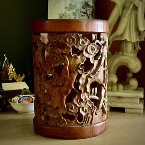 Peut inclure: Un récipient cylindrique en bois avec des motifs sculptés complexes. Le récipient est de couleur marron chaud et présente un motif détaillé de nuages tourbillonnants et d'autres formes. Les bords supérieur et inférieur sont d'un brun plus foncé.