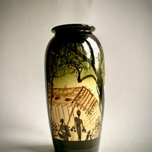 Peut inclure: Un vase en céramique noire avec une scène peinte à la main d'une hutte, d'arbres et de personnages. La scène est peinte dans des tons de brun, de vert et de blanc.