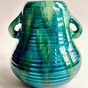 May include: A teal blue ceramic vase with two handles. The vase has a crackled glaze and a striped pattern.