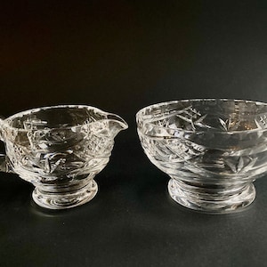 May include: A set of two clear glass sugar and creamer bowls with a cut glass design.