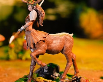 May include: A painted miniature figurine of a deer-like creature with antlers, a human-like torso, and a leafy crown. The figurine is brown and has a green base.