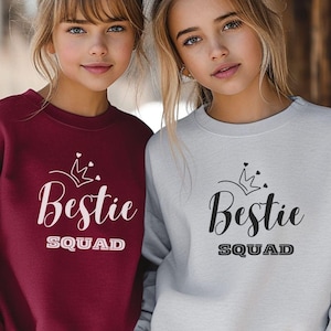 Puede incluir: Dos chicas con sudaderas a juego con el texto "Bestie Squad" y un gr&aacute;fico de corona. Una sudadera es burdeos y la otra es gris.