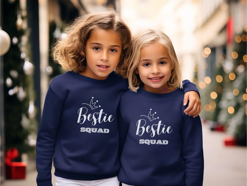 Puede incluir: Dos chicas con sudaderas azules marino a juego con una corona blanca y el texto "Bestie Squad".