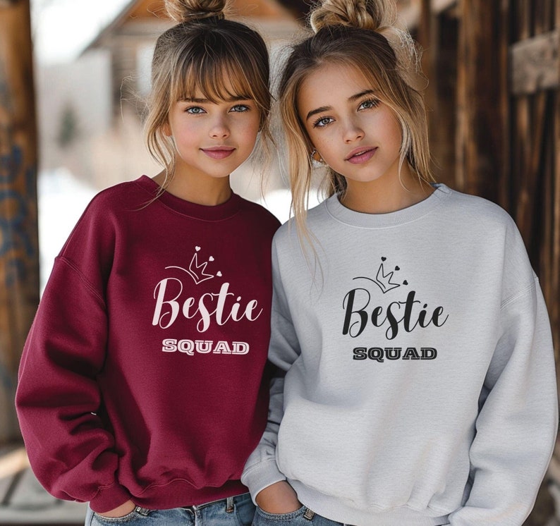 Puede incluir: Dos chicas con sudaderas a juego con el texto "Bestie Squad" y un gr&aacute;fico de corona. Una sudadera es burdeos y la otra es gris.