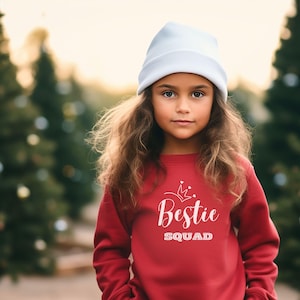 Puede incluir: Una persona joven con una sudadera roja con el texto "Bestie Squad" y un gr&aacute;fico de corona. Lleva una boina azul claro y tiene el pelo largo y casta&ntilde;o.