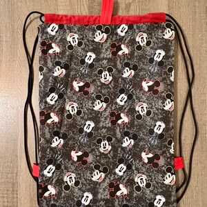 Puede incluir: Una bolsa de cord&oacute;n negro con ribete rojo y estampado de Mickey Mouse. La bolsa tiene un cierre de cord&oacute;n negro y est&aacute; hecha de un tejido duradero.