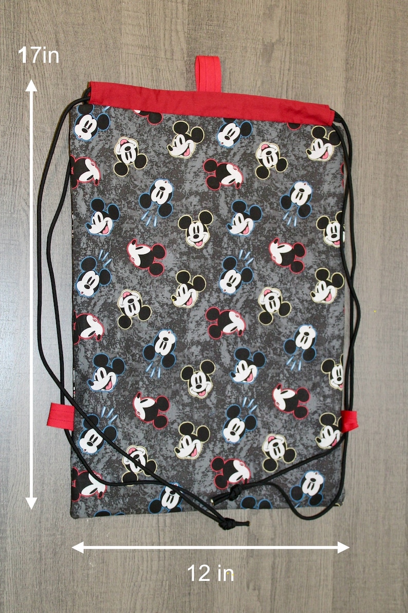 Puede incluir: Una bolsa de cord&oacute;n negro con la parte superior roja y un estampado de Mickey Mouse. La bolsa mide 43 cm de alto y 30 cm de ancho.