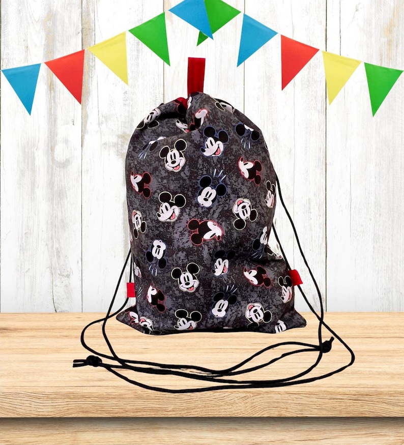 Puede incluir: Una bolsa de cord&oacute;n negro con estampado de Mickey Mouse. La bolsa tiene cordones negros y un acento rojo en la parte superior.
