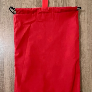 Puede incluir: Una bolsa de cord&oacute;n roja con un cord&oacute;n negro y una leng&uuml;eta roja.