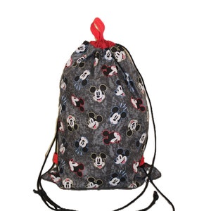 Puede incluir: Una bolsa de cord&oacute;n gris con un estampado de Mickey Mouse en blanco y negro. La bolsa tiene cordones rojos.