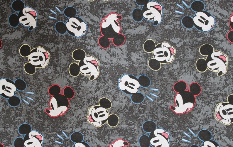Puede incluir: Una tela gris con un patr&oacute;n repetido de cabezas de Mickey Mouse en blanco y negro. Las cabezas de Mickey Mouse sonr&iacute;en y tienen la lengua fuera. Algunas de las cabezas de Mickey Mouse tienen acentos rojos, amarillos o azules.