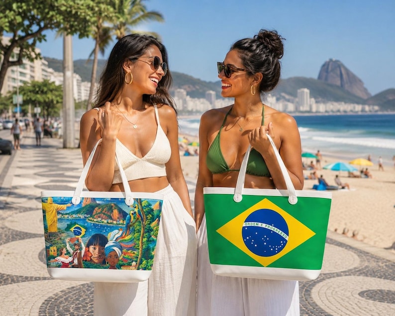 May include: Two women on a sunny beach holding tote bags. One bag features a colorful Brazilian landscape scene, the other displays the Brazilian flag. Both bags have white handles and trim. The women are wearing sunglasses and smiling.