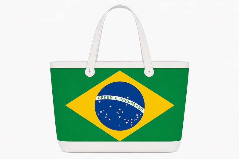 May include: A white-handled tote bag featuring the Brazilian flag. The bag's design includes a green background, a yellow diamond, and a blue circle with stars and text. The bag has a white base and handles.