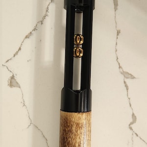 May include: A black and gold cue stick with a wooden handle. The top of the cue stick is black with a gold band. The middle section is black with gold accents. The bottom is a light brown wood.
