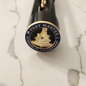 May include: A black object with a gold and blue emblem. The emblem reads "PAST MASTER" around the top, "WISDOM" on the left, and "LEADERSHIP" on the right. The emblem features a gold symbol with an eye.