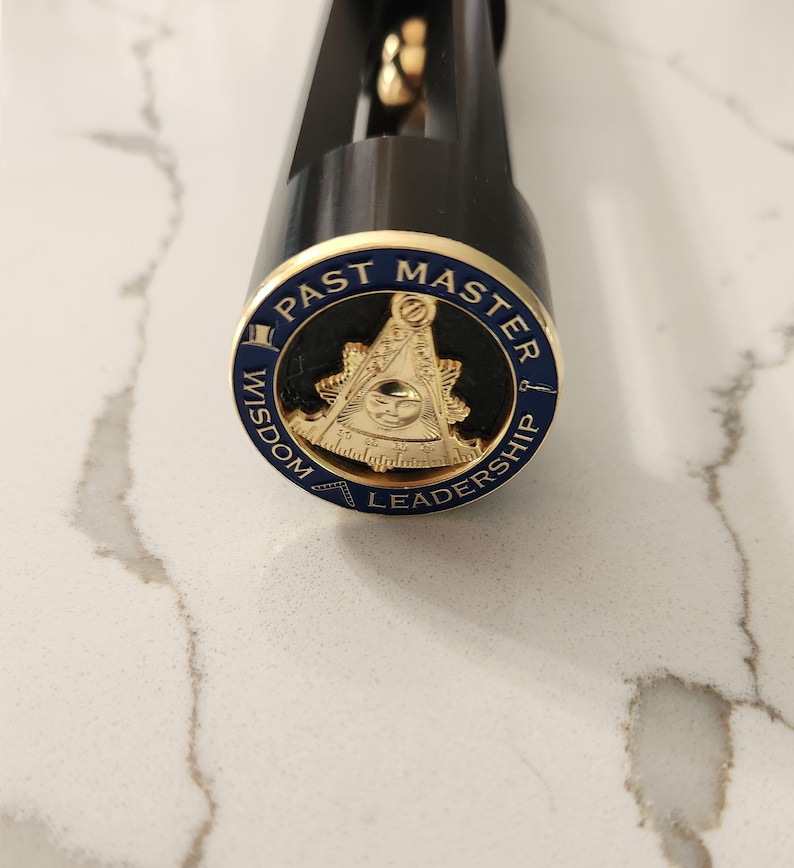 May include: A black object with a gold and blue emblem. The emblem reads "PAST MASTER" around the top, "WISDOM" on the left, and "LEADERSHIP" on the right. The emblem features a gold symbol with an eye.