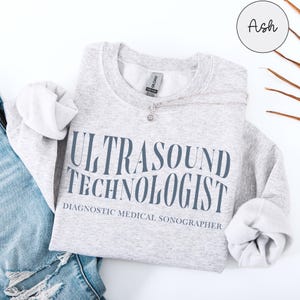 Peut inclure: Un sweat-shirt gris avec le texte "Ultrasound Technologist Diagnostic Medical Sonographer" en lettres bleues.