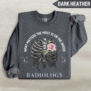 May include: Dark heather grey sweatshirt with a ribcage graphic and a pink rose inside. The text "What matters the most is on the inside" is written around the ribcage graphic. The text "Radiology" is written below the graphic.