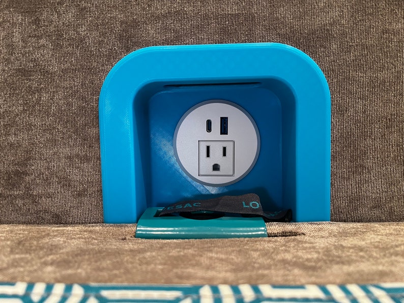 May include: A blue plastic outlet cover with a standard US electrical outlet and two USB ports. The cover is mounted on a brown fabric surface.