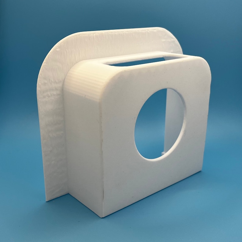 May include: White plastic wall mount with a round opening and a rectangular slot. The mount is designed to hold a device or object.