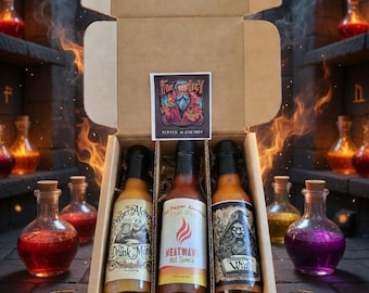 Puede incluir: Una caja de cartón que contiene tres botellas de salsa picante. Las etiquetas presentan ilustraciones y texto, incluyendo "Drunk Monk", "Heatwave" y "Wrath". Una pegatina en la caja dice "Star Sncy Pepper Alchemy".