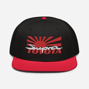 Puede incluir: Gorra de béisbol negra y roja con un sol naciente rojo y bordado blanco "Supra Toyota".
