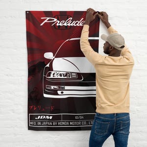 May include: A red and black flag with a white silhouette of a Honda Prelude car. The flag has the text "Prelude" and "JDM" in white. The text "プレリュード" is in Japanese. The flag also has the text "10/94" and "MFD. IN JAPAN BY HONDA MOTOR CO., LTD".