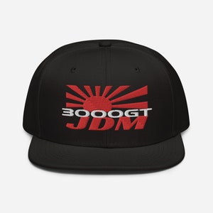 Op de afbeelding: Zwarte baseballpet met een geborduurd Japans zonsopgangontwerp in rood en wit en de tekst "3000GT JDM".