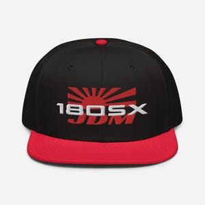 Puede incluir: Gorra de béisbol negra y roja con un logotipo bordado en blanco que dice "180SX JDM" y un gráfico de sol naciente rojo.