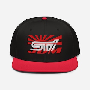 May include: Black and red baseball cap with a flat brim. The cap features a red and white graphic design with the text "JDM" in red. The cap has a red button on top.