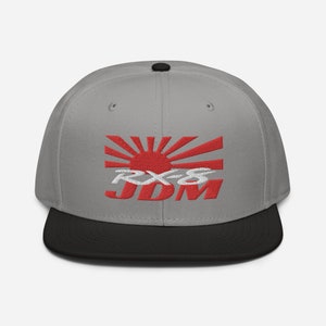 May include: A grey and black baseball cap with an embroidered red rising sun and the text "RX-8 JDM" in white.