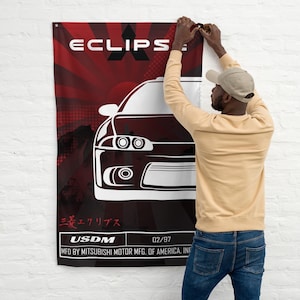 Peut inclure: Un drapeau mural rouge et noir avec un contour blanc de voiture et le mot "ECLIPS" en blanc. Le drapeau comprend également du texte japonais et le texte "USDM 02/97 MFD BY MITSUBISHI MOTOR MFG. OF AMERICA, INC."