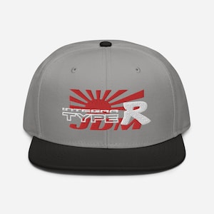 May include: A grey and black baseball cap with a red and white rising sun graphic and the text "Integra Type R JDM" embroidered on the front.
