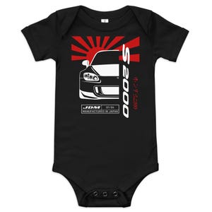 May include: Black baby bodysuit with a white graphic of a car, the text "S2000", and a red rising sun design. The text "JDM 07/04 MANUFACTURED IN JAPAN" is also included.