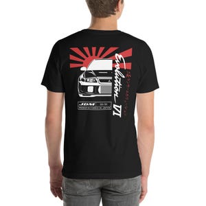 Puede incluir: Camiseta negra con un gráfico blanco de un Mitsubishi Lancer Evolution IV con una bandera japonesa y el texto "Evolution IV" y "JDM 08/96 MANUFACTURED IN JAPAN" en blanco.
