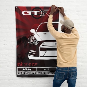 Peut inclure: Une illustration en noir et blanc d'une voiture Nissan GT-R R35 sur un fond rouge et noir. Le texte "GTR", "日産GT-R R35", "JDM", "09/12", et "MFD. IN JAPAN BY NISSAN MOTOR CO., LTD" est imprimé sur l'image.