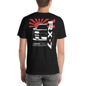 May include: Black t-shirt with a white graphic of a car, a rising sun, and the text "RX-7", "JDM", "02/95", and "MANUFACTURED IN JAPAN".