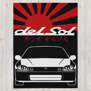 May include: Black and red throw blanket featuring a white car graphic. The blanket has the text "del Sol" in white, with Japanese characters and a red sunburst design. The car graphic is a front view of a Honda Del Sol.