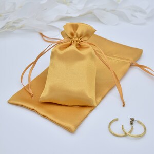 May include: A gold satin drawstring bag with a matching satin pouch. The bag is lying on a white surface.
