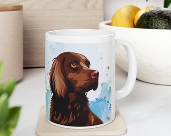 Könnte beinhalten: Eine weiße Keramiktasse mit einer braunen und weißen Illustration eines Hundekopfes auf einem blauen Aquarellhintergrund. Der Hund schaut nach rechts im Bild.