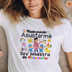 Puede incluir: Camiseta blanca con un diseño gráfico colorido que dice "Nada puede asustarme Soy maestra de preescolar". El diseño incluye una maestra y niños, un arcoíris, una mariposa, un sol, una pelota y otros elementos coloridos.