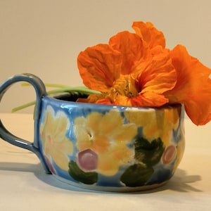 May include: A blue and yellow ceramic mug with a floral design and a single orange flower inside.