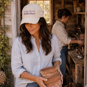 Puede incluir: Una gorra de béisbol beige con el texto bordado Executive Dysfunction Motherhood en azul oscuro. La gorra tiene una visera curva y una corona estructurada, ofreciendo un aspecto clásico. Está hecha de una tela de color claro con costuras visibles.