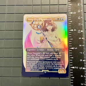 May include: A holographic trading card featuring "Yuna, Grand Summoner." The card depicts an anime-style character with brown hair and a staff. Text includes "Legendary Creature - Human Cleric" and game instructions. The card is approximately 3.5 inches tall.