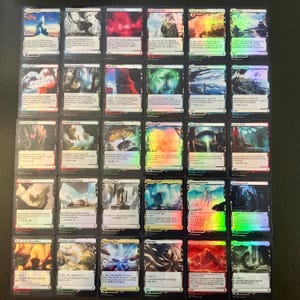 May include: A collection of Magic: The Gathering trading cards, featuring various landscape and character illustrations. The cards have a holographic sheen and are arranged on a dark surface. Each card displays unique artwork and text.