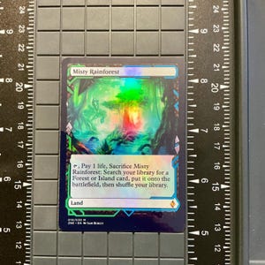 May include: A collectible card titled "Misty Rainforest" with a vibrant, colorful illustration of a rainforest scene. The card features text describing its function in a card game. The card is set against a black background with measurement markings.