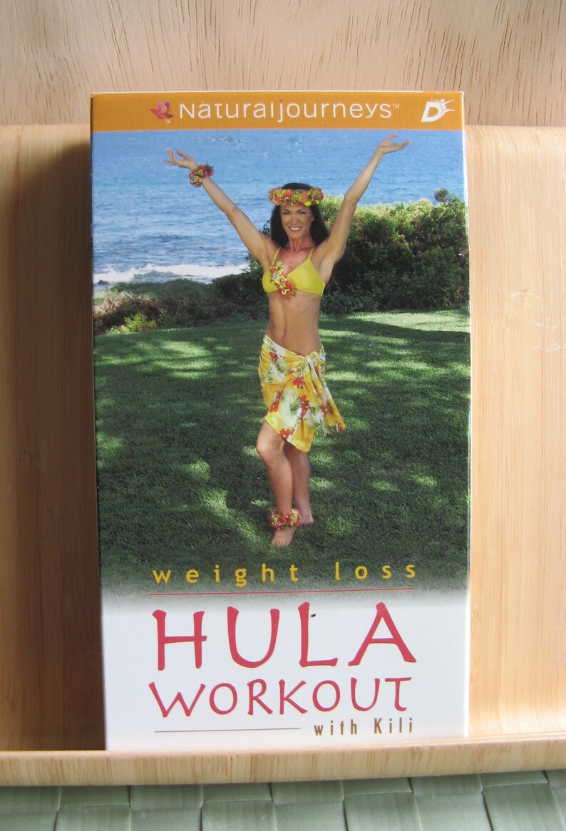 Peut inclure: Une jaquette de DVD pour une vid&eacute;o d'entra&icirc;nement de hula avec une femme en jupe florale jaune et orange et un haut de bikini jaune. La jaquette est blanche avec du texte rouge qui dit "HULA WORKOUT with Kili" et "weight loss". L'arri&egrave;re-plan est une zone herbeuse verte avec une mer bleue au loin.
