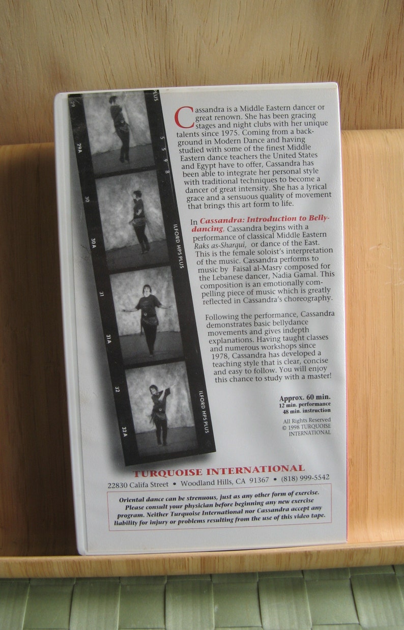 Peut inclure: Une cassette VHS en noir et blanc mettant en sc&egrave;ne une danseuse orientale. La cassette est intitul&eacute;e "Cassandra : Introduction &agrave; la danse du ventre". La couverture comprend une s&eacute;rie de photos en noir et blanc de la danseuse dans diff&eacute;rentes poses. Le texte sur la couverture indique "Approx. 60 min. 12 min. performance 48 min. instruction. All Rights Reserved &copy; 1998 TURQUOISE INTERNATIONAL."
